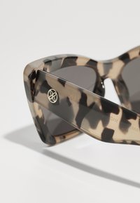 Tortoiseshell sunglasses with a thick frame, featuring dark gradient lenses and a small gold logo on the temple. Textured finish.