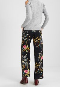 Blumenmusterweite Hosen in Schwarz mit bunten Designs von Rosen und Grünpflanzen. Abgerundet durch eine glatte Stofftextur.