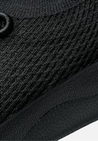 Svart sko med texturerad stickad ovandel och en slät gummisula med ett mönster av upphöjda punkter. Hållbara material säkerställer en bekväm passform.