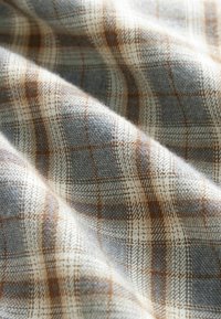Soft woven fabric in light beige with a plaid pattern in grey and brown. It displays a smooth texture and a subtle sheen.