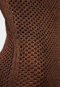 Κοντινή λήψη λεπτομερούς καφέ πλεκτού υφάσματος με υφή ανοιχτής ύφανσης και κάθετες στερεές πλεκτές γραμμές.