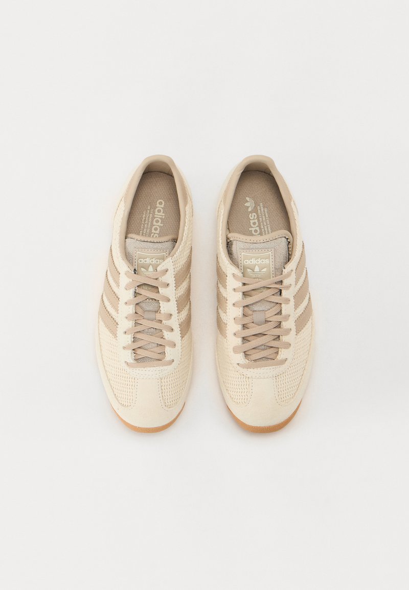 Baskets de sport beiges avec une tige en textile et en cuir suédé, trois bandes marron, fermeture à lacets et semelle en caoutchouc. Design classique et profil bas.
