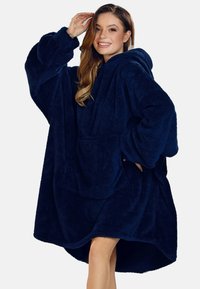 Námořnická modrá oversized kapucínová deka vyrobená z plyšového materiálu, s velkou přední kapsou a širokými rukávy pro pohodlí a teplo.