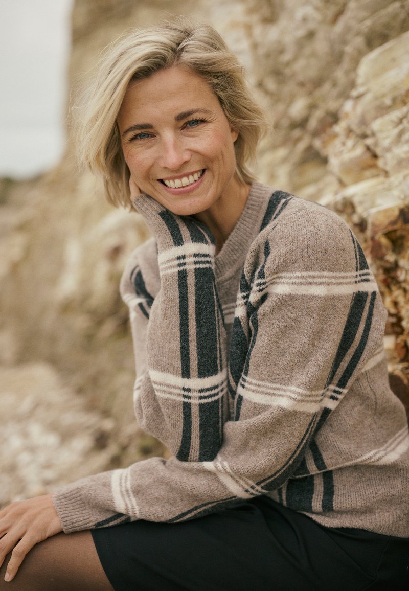 Hellbrauner Pullover mit dunkelblau-weißem Karomuster, leichtem Stoff, gerippten Bündchen und Rundhalsausschnitt, kombiniert mit einem schwarzen Rock.