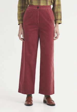 Persona que lleva pantalones de pana rojos de cintura alta y pata ancha, camisa de cuadros verde de manga larga, calcetines a rayas y mocasines de cuero marrón.