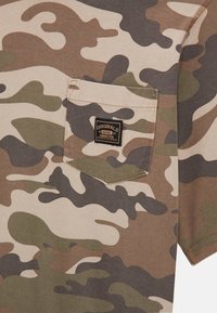 Korte mouwen shirt met camouflagedessin in beige, bruin en groen. Heeft een borstzak met een zwart label en een zachte katoenstructuur.