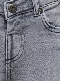 Primo piano di jeans in denim grigio chiaro che mostrano la tasca anteriore, il passante per cintura e il bottone metallico con incisione del marchio.