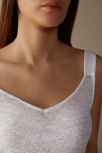 Bílý, lehký top na ramínka s V- výstřihem a tenkými pásky. Materiál má mírně průsvitnou strukturu, která vystihuje minimální detaily šití.