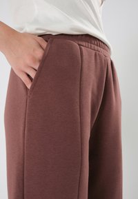 Braune Sweatpants mit softem Material, ausgestattet mit einem elastischen Bund und seitlichen Taschen. Der Stoff hat eine leicht gebürstete Oberfläche.