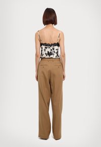 Black floral lace-trimmed camisole over beige high-waisted trousers. The trousers feature two back pockets and a relaxed fit.
