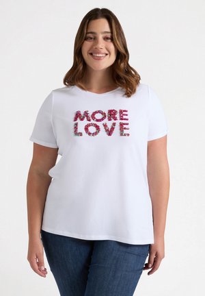Weißes T-Shirt mit kurzen Ärmeln und dem Schriftzug "MORE LOVE" in buntem Blumenapplikationen. Lässiger Schnitt, runder Ausschnitt, kombiniert mit blauen Jeans.