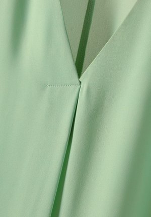 Mintgroene blouse met een V-hals ontwerp. Kenmerkt zich door gladde, lichte stof en nette stiksels langs de naden.