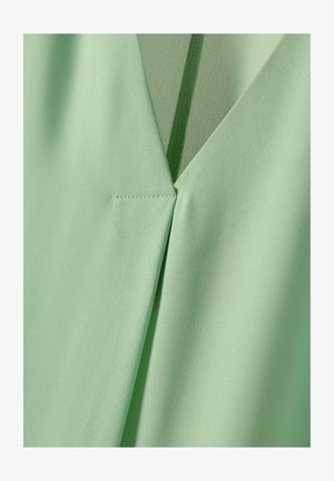 Mintgroene blouse met een V-hals ontwerp. Kenmerkt zich door gladde, lichte stof en nette stiksels langs de naden.