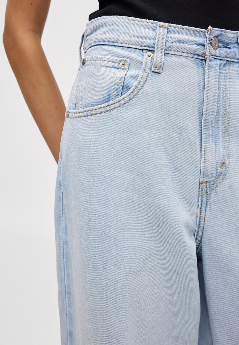 Lyseblå denimjeans med høj talje, udstyret med lynlås, forlommer og kontrastfarvet syning langs sømmene.