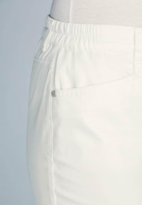 Pantalons blancs élastiqués avec une poche latérale dotée d'un bouton-pression argenté, fabriqués en tissu doux et lisse au design minimaliste.
