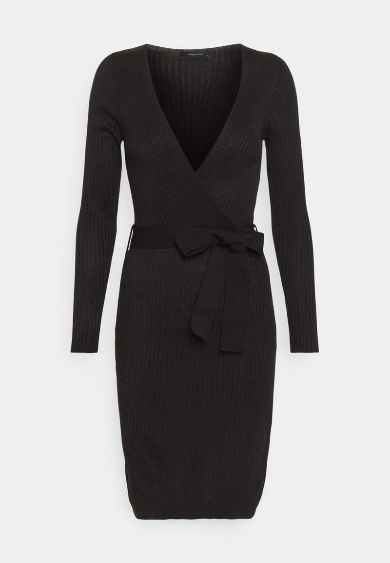 Robe noire côtelée avec un col en V profond, manches longues et ceinture à la taille. Le tissu a une finition texturée et une coupe moulante.