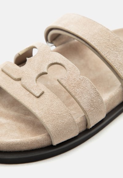 Μπεζ σουέντ σανδάλι με δύο λουράκια, το ένα με διακοσμητικό σχέδιο με κοψίματα, και μαύρη σόλα.