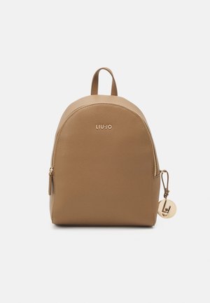 Beżowy plecak ze szorstkiej skóry z złotym zamkiem błyskawicznym, górnym uchwytem i okrągłym złotym zawieszonym na boku breloczkiem z logo.