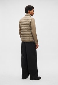 Veste matelassée beige avec design matelassé, col montant et poignets élastiques, associée à un pantalon noir ample et des chaussures noires.