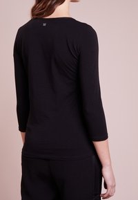 Schwarzes Shirt mit drei Viertelärmeln aus weichem Stoff, mit einem runden Ausschnitt und einem kleinen Logodetail auf der Rückseite.