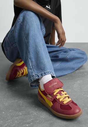 Baskets rouges et jaunes avec une tige texturée, des accents en suède, une sangle Velcro et une semelle en caoutchouc, portées avec un jean en denim bleu ample.