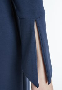 Manche de robe bleu marine avec détail de fente sur le côté, en tissu lisse, présentant une coupe décontractée et des lignes épurées.