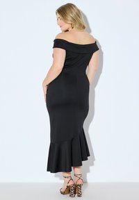 Czarna sukienka odkrywająca ramiona, z dopasowanym gorsetem, rozszerzanym dołem i fakturowaną tkaniną. Dobierz do niej sandały na obcasie w panterkę z paskami.