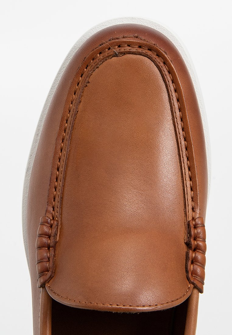 Mocassin en cuir marron avec des coutures détaillées et une semelle blanche, présenté de haut sur un fond uni.