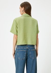 Camisa corta verde claro con mangas cortas, fabricada en tejido texturizado y con cuello, combinada con unos jeans de mezclilla azul de talle alto que cuentan con dos bolsillos traseros.