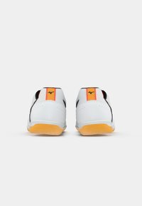 White athletic shoes with a smooth texture, featuring black accents and a bright orange and red stripe at the heel. Rubber outsole.