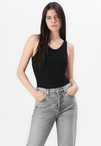 Zwarte geribbelde body met brede banden, gecombineerd met lichtgrijze hoge taille spijkerbroek. De spijkerbroek heeft voorzakken en een klassieke pasvorm.