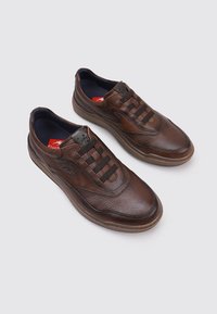 Zapatillas de cuero marrón con parte superior texturizada, cordones elásticos y cuello acolchado. Presentan una suela oscura en contraste y un detalle de logo en el lateral.