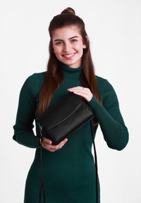 Černá kožená křížová taška s texturovanými panely, přední klopou a odnímatelným ramenním popruhem. Obsahuje nenápadnou detail s logem.