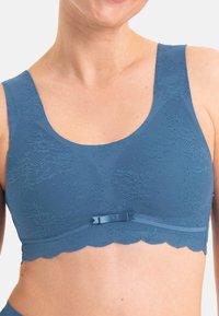 Bralette en dentelle bleue avec des larges bretelles, des bords festonnés et un nœud décoratif au centre. Fabriqué à partir d'un matériau doux et texturé.