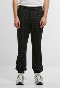 Sorte joggebukser med et subtilt logomønster, elastisk midje og mansjetter. Stoffet ser mykt og behagelig ut. Kombinert med lyse joggesko.