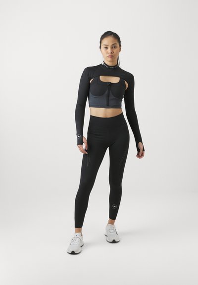 Conjunto deportivo negro que incluye una camiseta de manga larga con diseño recortado y leggings de cintura alta. Tejido suave y elástico con detalles decorativos.