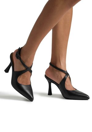 Scarpe nere in pelle con tacco alto, punta affusolata, design con ritagli laterali e cinturini alla caviglia regolabili, con un piccolo accento decorativo.