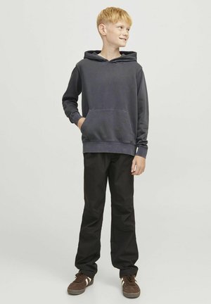 Sweatshirt à capuche gris foncé avec poche avant, associé à un pantalon noir et des baskets marron, avec des rayures blanches sur les côtés.