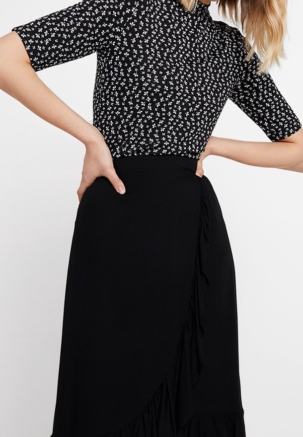 Vestido negro de manga corta con un pequeño patrón floral blanco. La falda tiene un acento con volantes en el lado y un diseño cruzado.