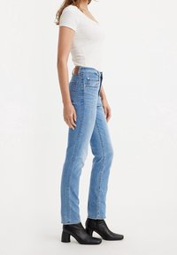 Jeans ajustados de color azul claro con una cintura alta y un diseño clásico de cinco bolsillos, combinados con una blusa ajustada de canalé blanca y botas negras de tacón bloque.