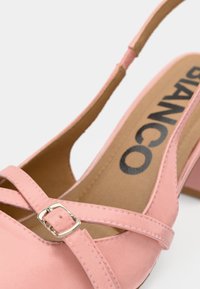 Ροζ παπούτσι τύπου slingback με σατινέ φινίρισμα, διαθέτει λουράκια που διασταυρώνονται και ασημένια αγκράφα. Κλειστή μύτη με μικρό, χοντρό τακούνι.