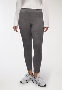 Leggings grigi realizzati in un tessuto elasticizzato, con una vita alta per maggiore supporto, abbinate a scarpe da ginnastica bianche e grigie.