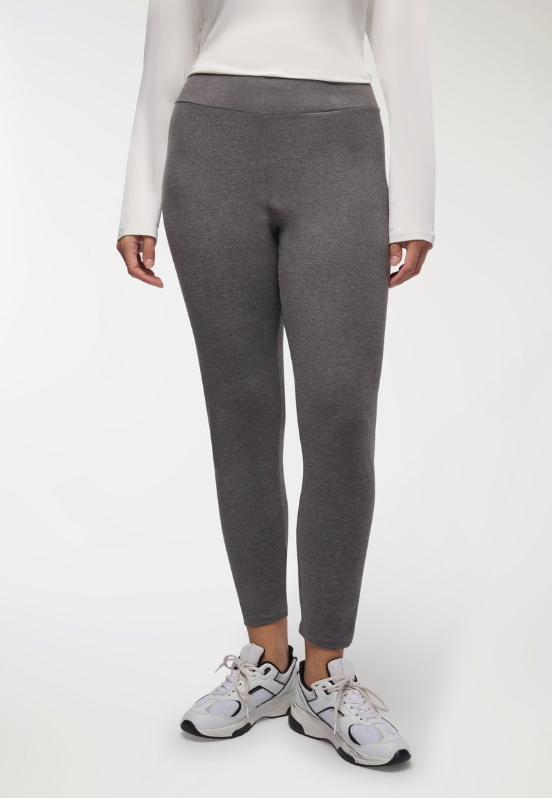 Leggings grigi realizzati in un tessuto elasticizzato, con una vita alta per maggiore supporto, abbinate a scarpe da ginnastica bianche e grigie.