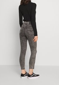 Högt midjade svarta denimjeans med en urtvättad textur och hjärtformade bakfickor, kombinerade med svarta sneakers och en långärmad topp.