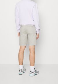 Shorts gris clair en tissu doux, à coupe droite et deux poches arrière, portés avec un sweat-shirt violet et des baskets grises.