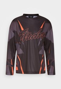 Svart långärmad skjorta i lätt material med orange detaljer och ett stjärnmönster. Framsidan har en framträdande logotypdesign.