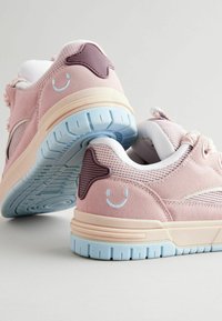 Różowe zamszowe sneakersy z siateczkowym detalem, kremową podeszwą środkową i niebieską gumową podeszwą. Posiadają wzór uśmiechniętej twarzy oraz fakturowane akcenty.