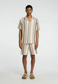 Ριγέ πουκάμισο με κοντά μανίκια και ταιριαστό σορτς σε αποχρώσεις μπεζ, καφέ και γκρι· ελαφρύ ύφασμα· casual σχεδιασμός· φλατ σανδάλια.