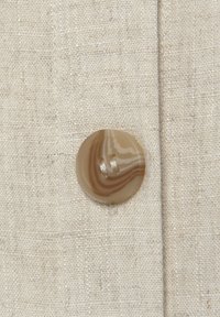 Beige linen fabric featuring a large, round, marbled button with a striped pattern and two needle holes near the edge.