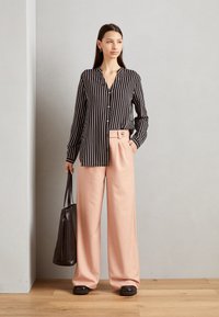 Black and white striped button-up shirt paired with light pink high-waisted wide-leg trousers; holding a black leather tote bag.